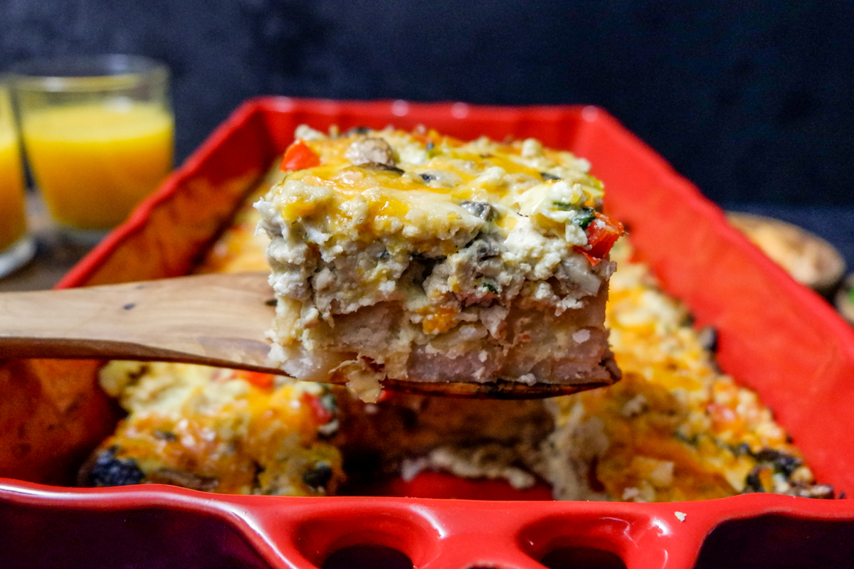 hashbrown breakfast casserole slice above red casserole dish on a wooden serving spoon