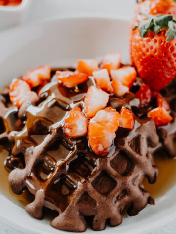 chocolate protein waffle in a shall bowl with strawberries and syrup