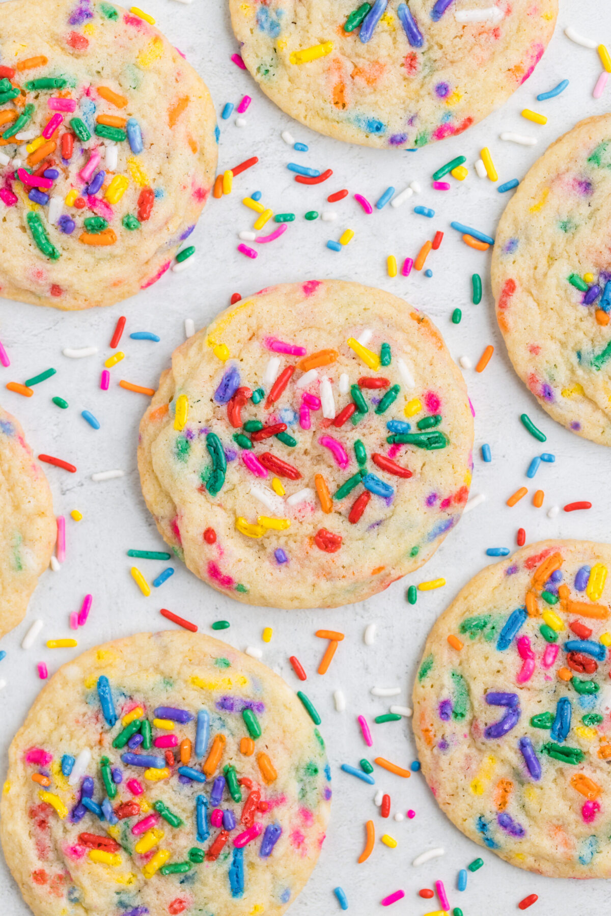 7 cookies spread out on a white surface with sprinkles all around them.