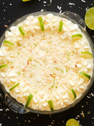 no bake key lime pie whole with lime slices, whipping cream frame and topped with sprinkled toasted coconut