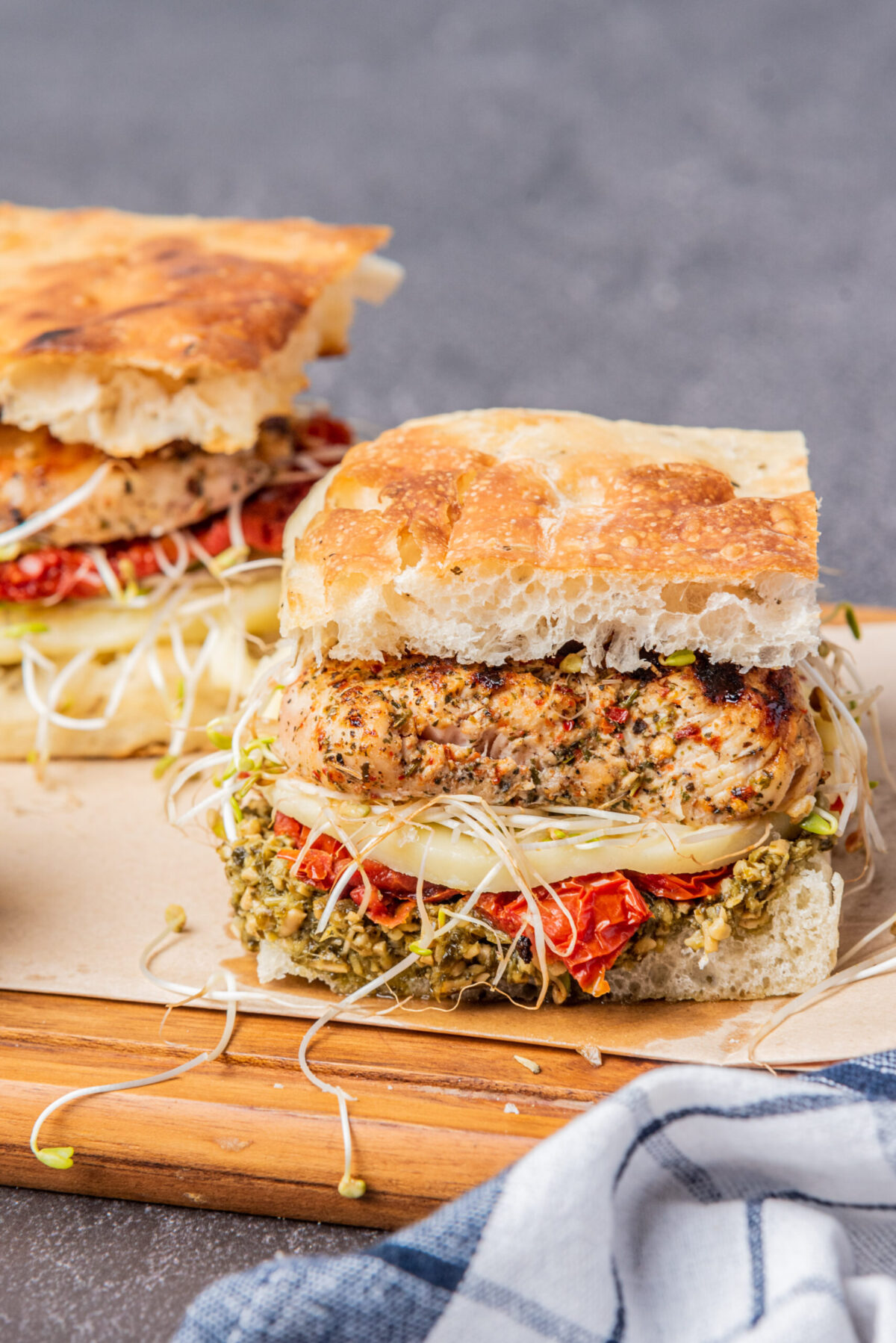 two assembled sandwiches on focaccia with sprouts on a wood board